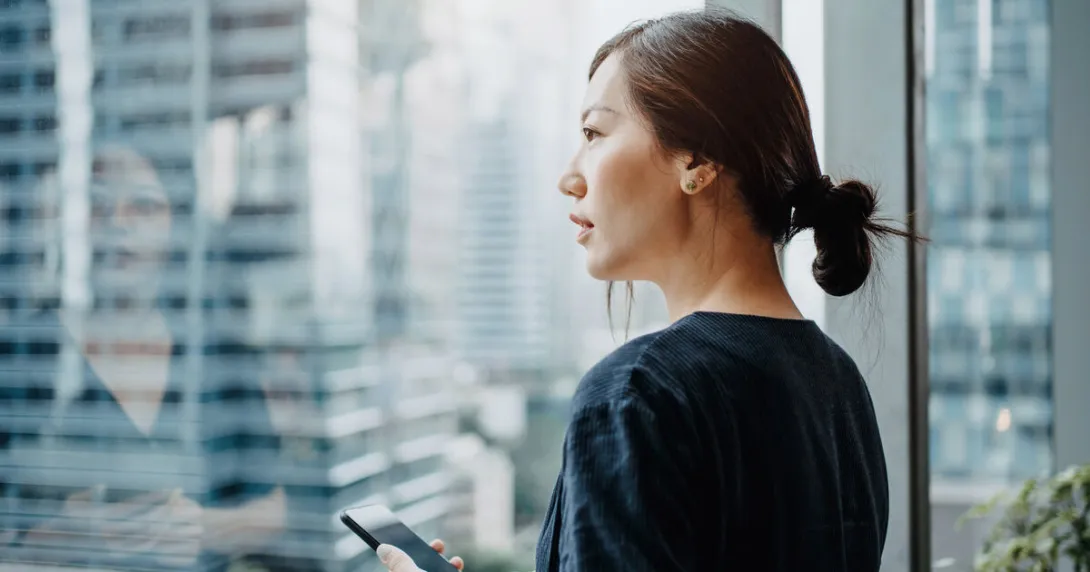 A woman holding a smartphone staring out the window