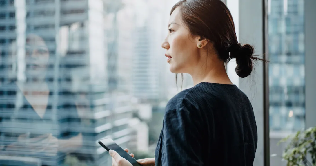 Person standing inside a building looking out a glass window at a big city
