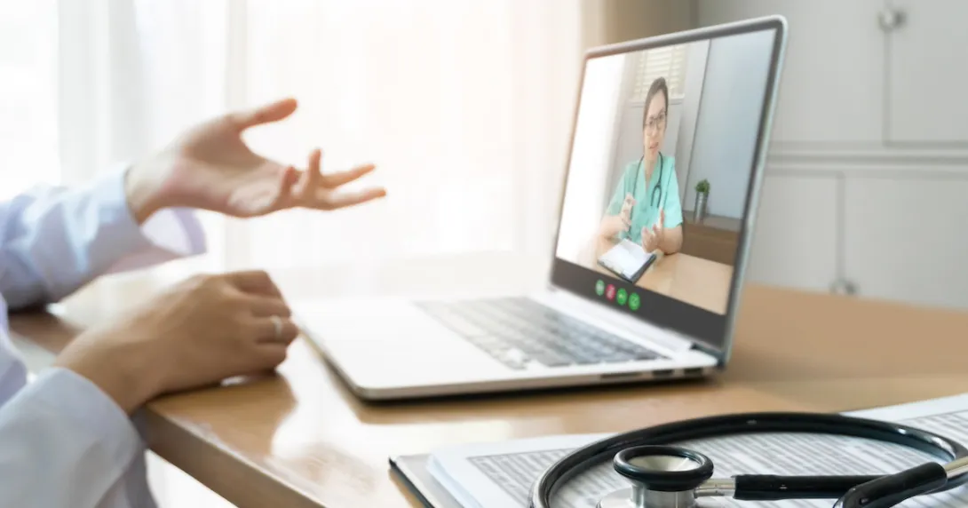 Healthcare provider sitting at a desk with a computer on it and a person on the screen