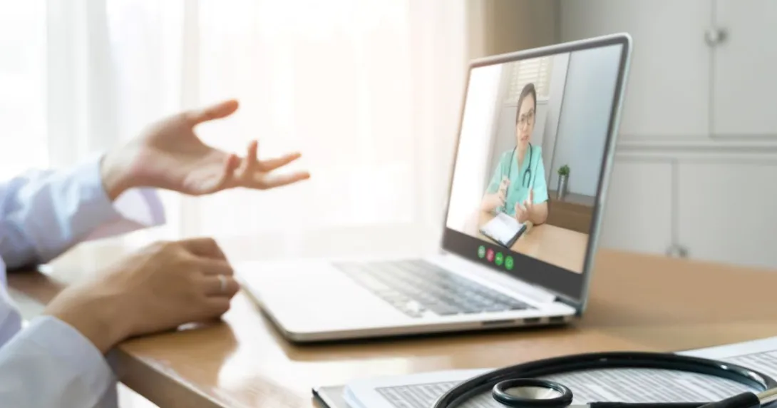Person in lab coat talking with hands to nurse on laptop