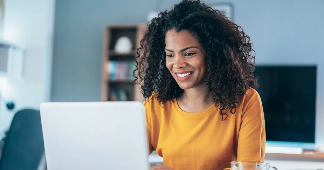 Person sitting at a table while looking at a computer and smiling