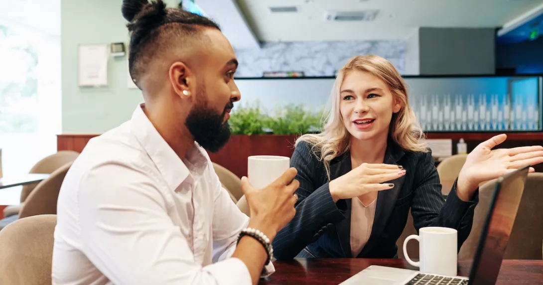 Two people sitting at a table while talking and looking at a computer