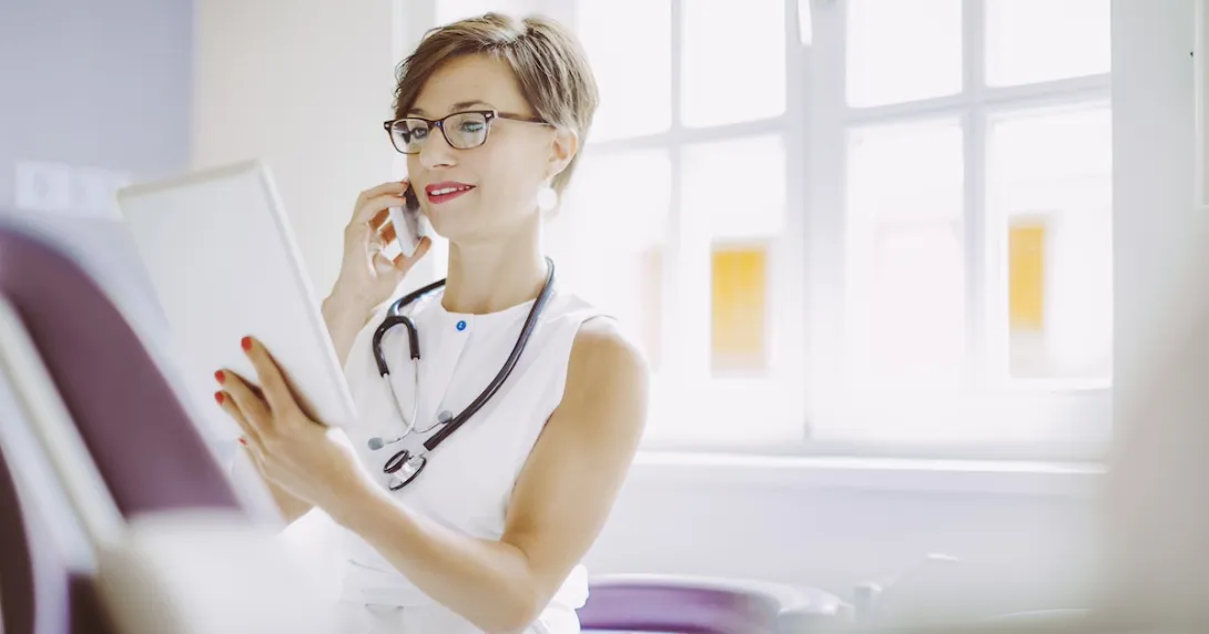 Healthcare provider sitting in an office wearing a stethoscope and looking at a tablet