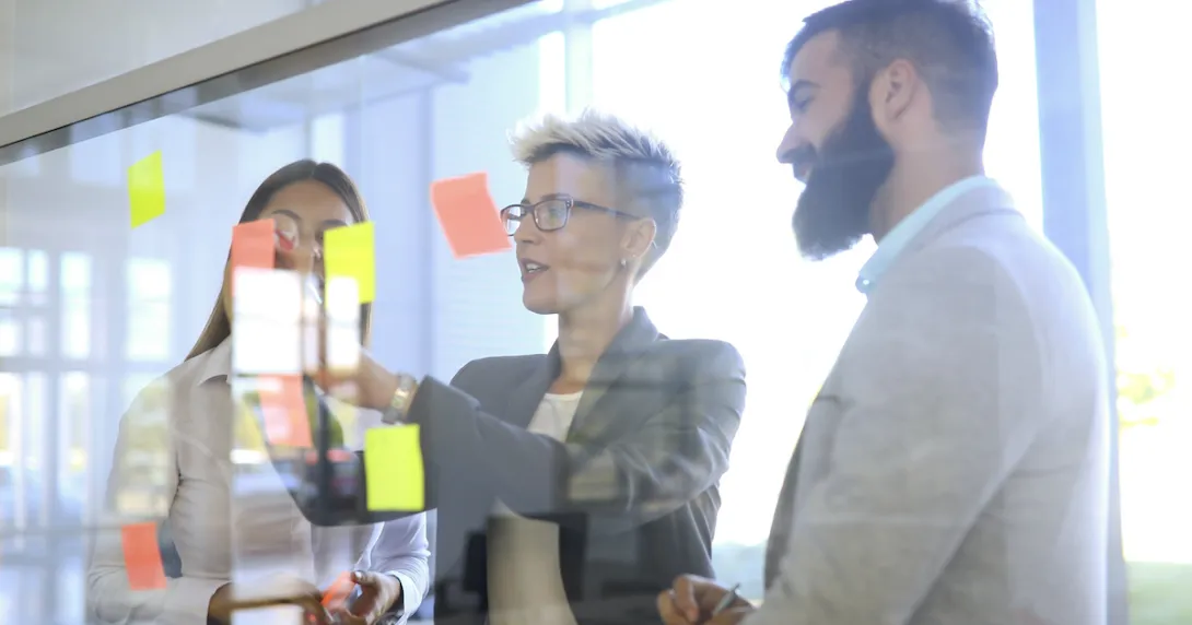 Three people standing in front of a board looking at post-its on a wall