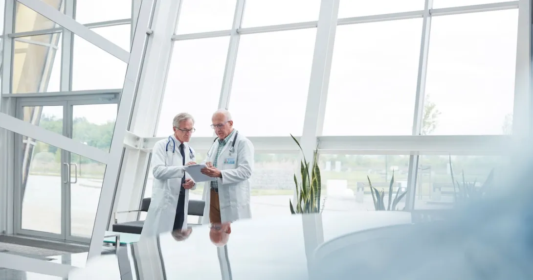 Two healthcare providers standing in a room in front of large windows