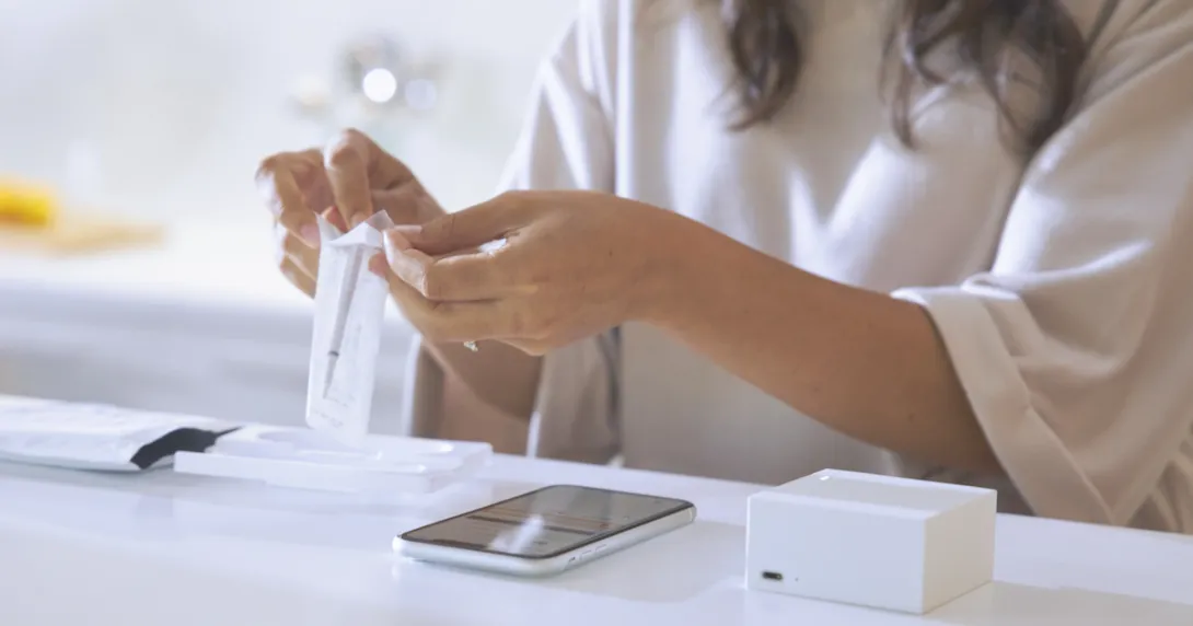 A woman removing the Cue wand from its package with a smartphone and Reader on the table in front of her