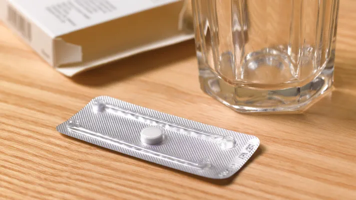 Moring after pill in its packaging on a table next to an empty glass