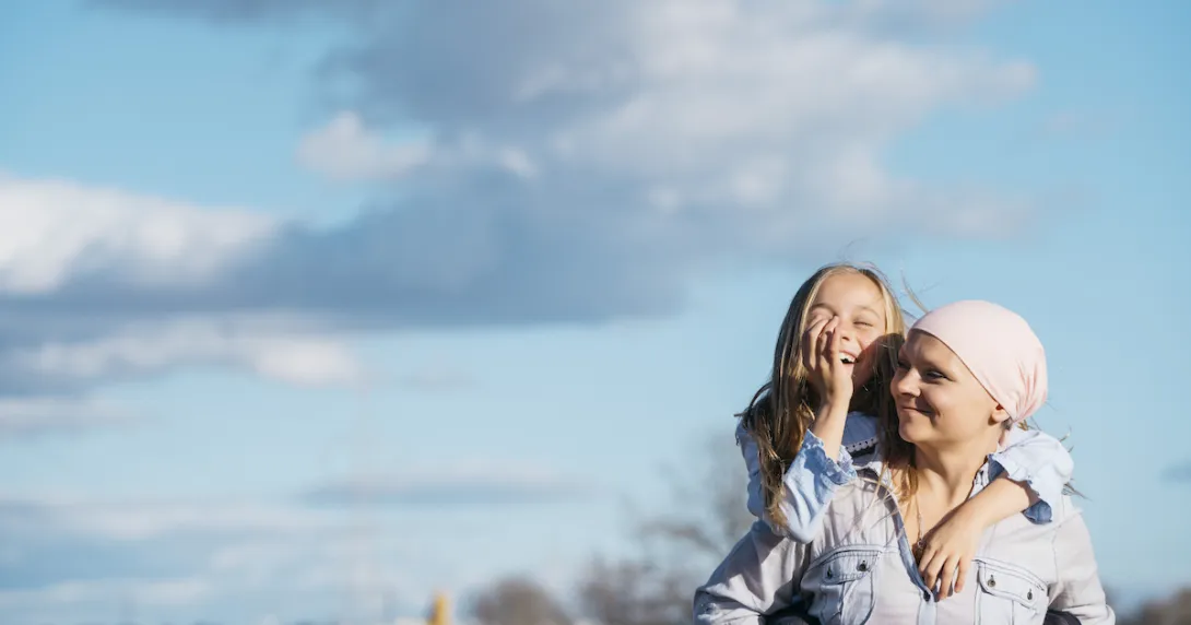 Person wearing a scarf on their head holding a child on their back with the sky behind them