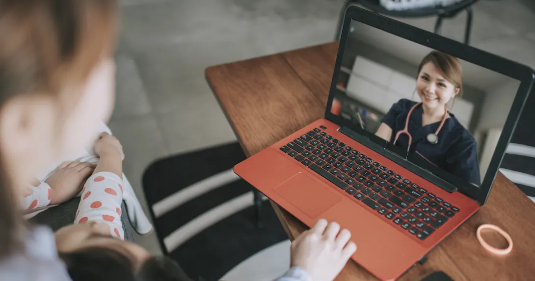 Person sitting down while looking at an orange and black laptop with a healthcare provider on the screen