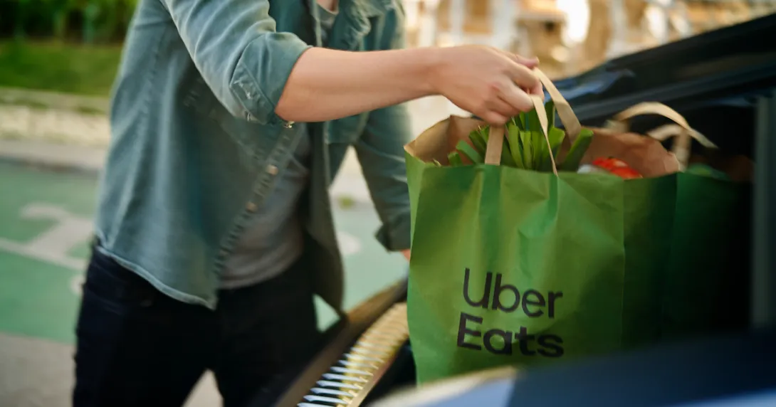 Person putting a bag of groceries from Uber Eats in a car's trunk