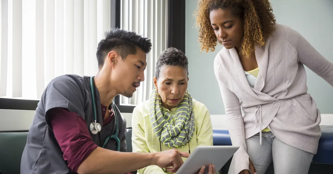 A doctor looking at data on a tablet with a patient and her family member.