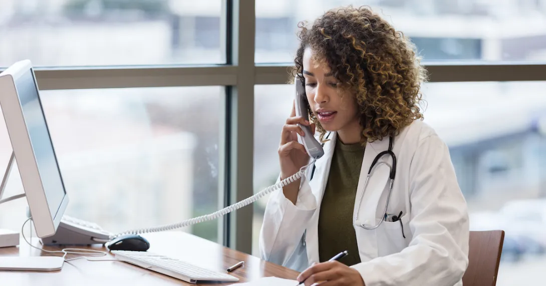 A doctor talking to a patient on a landline phone while taking notes.