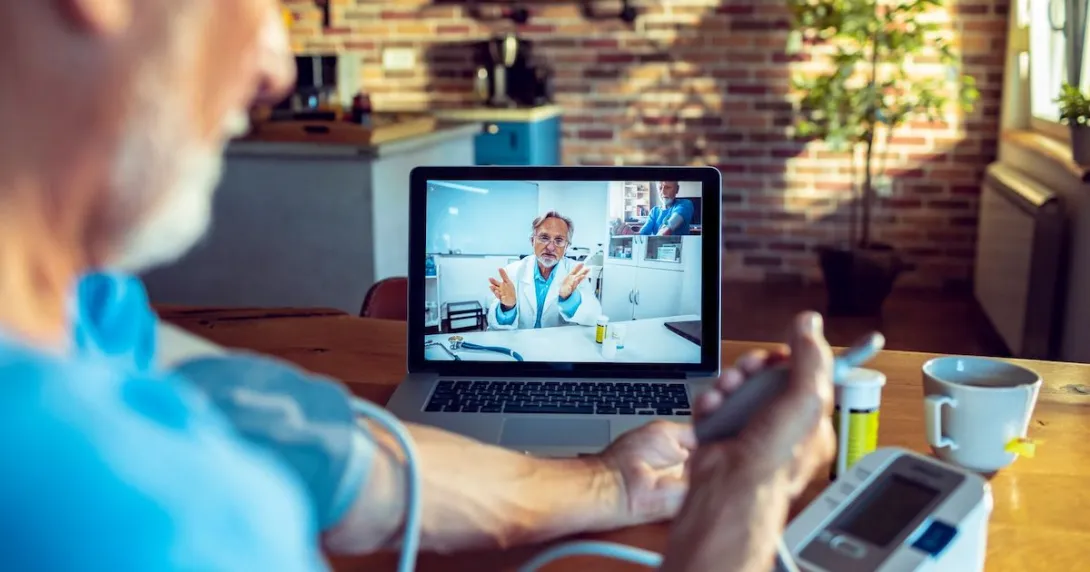A patient talking to a doctor through a video chat on his computer while using a connected blood pressure device.