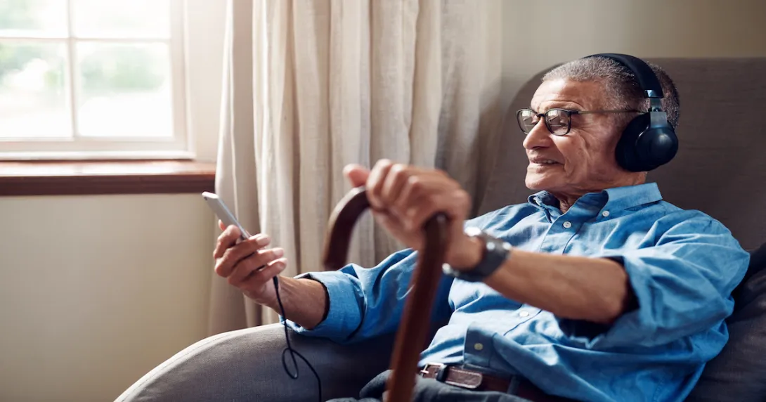 An older man sitting in his home using a smartphone.