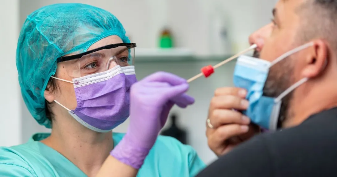 Female doctor in protective workwear taking nose swab test from middle aged man wearing protective face mask
