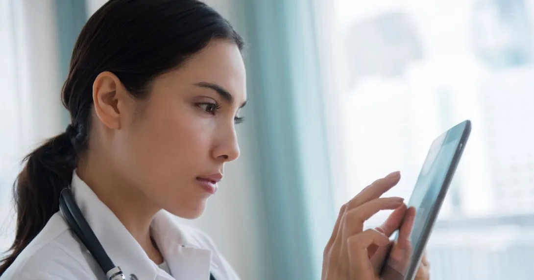 Healthcare provider wearing a lab coat and a stethoscope while interacting with a tablet