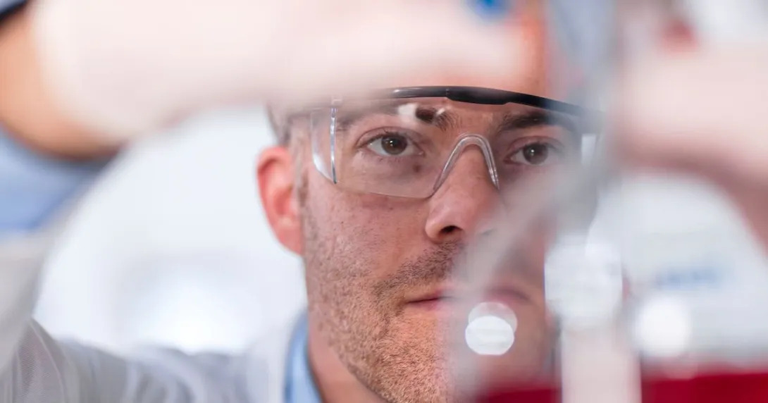 Scientist in a laboratory filling up a beaker while wearing safety goggles