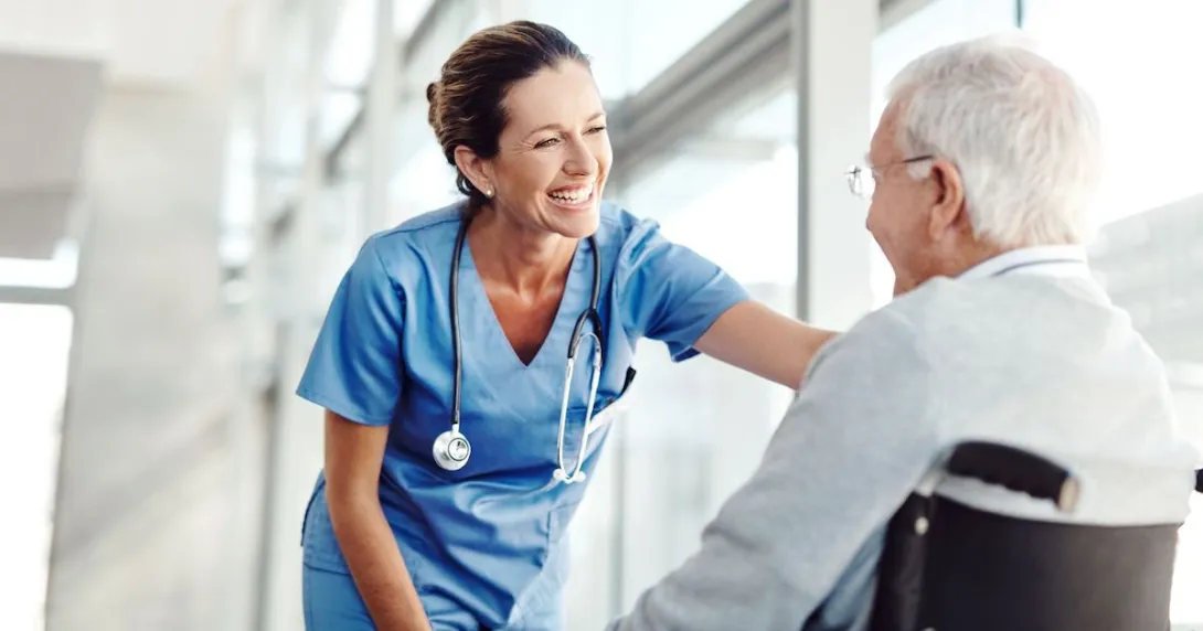 Person sitting in a wheelchair with a healthcare provider in scrubs standing over them