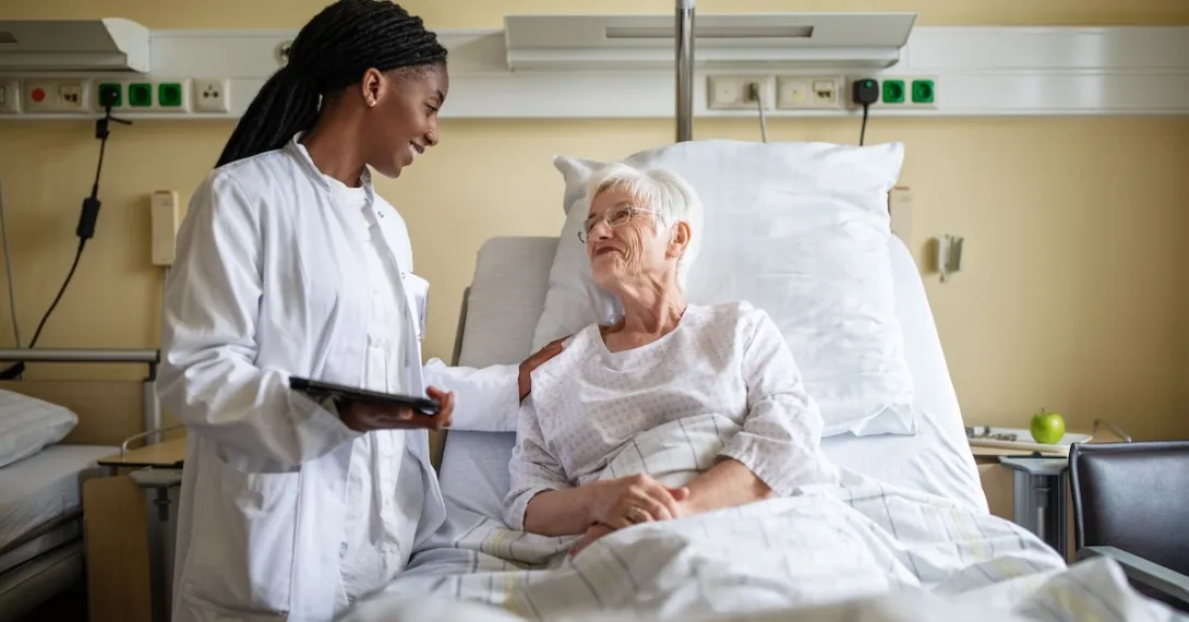 Healthcare provider standing next to a patient lying in a bed in a hospital room