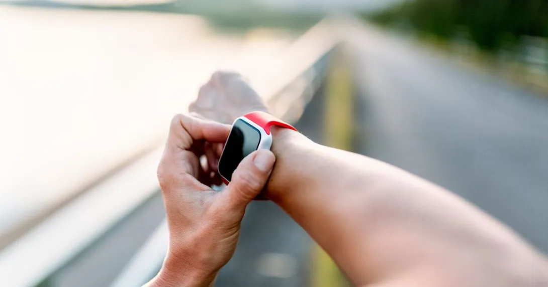 A person wearing a wearable device on their right wrist and touching the device with their left hand