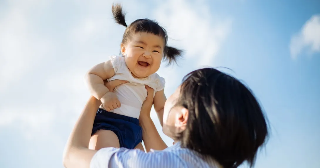 Person holding another little person above their head with the sky in the background