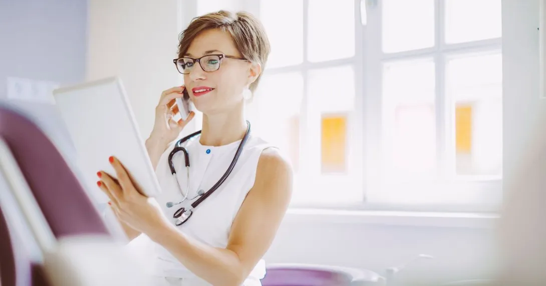 A doctor calling a fellow from their mobile phone while reviewing a patient's file on a digital tablet