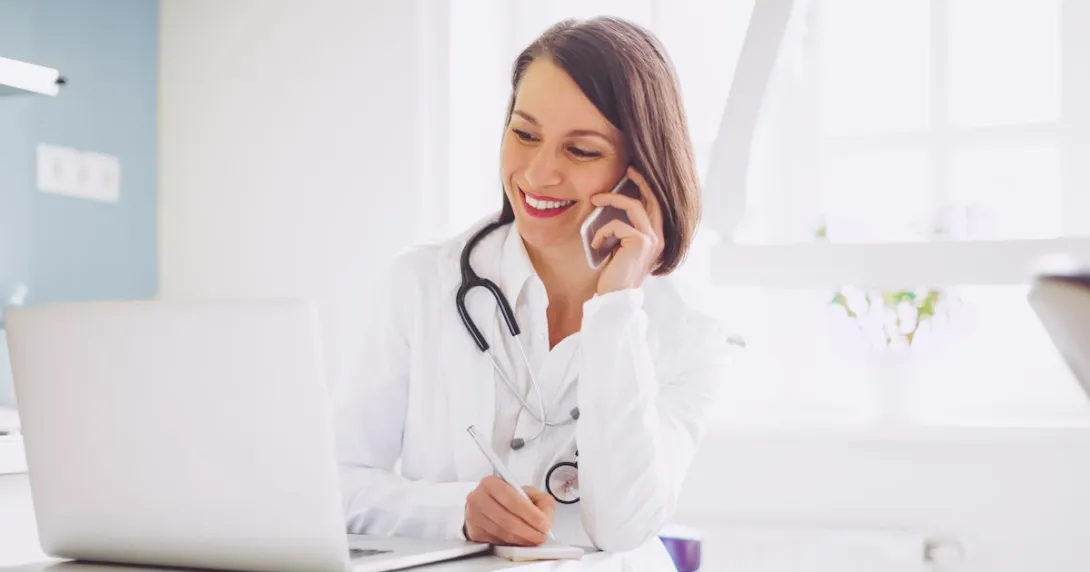 A doctor on the phone with a patient while checking their medical record on a laptop computer