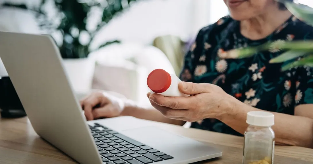 A woman holding a pill bottle using a laptop