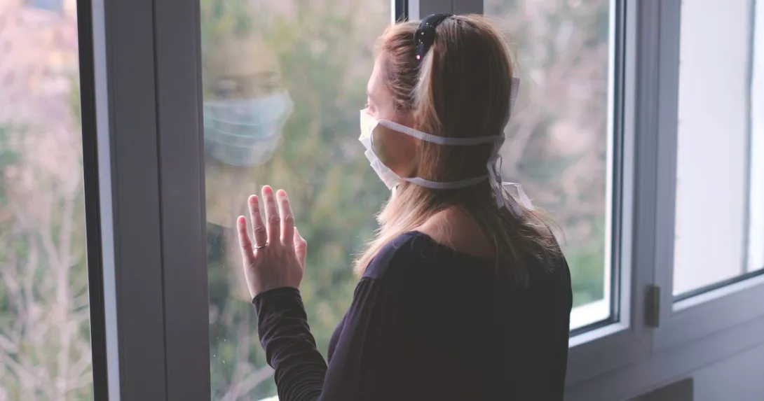 A woman wearing a mask looking out a window